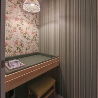 グリーンを基調とした、北欧風の授乳室の写真。 おむつを替えるための広いマットが、腰くらいの高さに設けられており、授乳用のいす、ウェットティッシュ、タオルが用意されている。