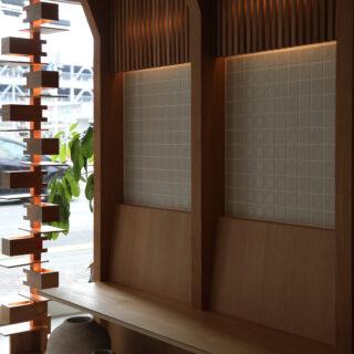 エントランスに造作されたベンチの写真。 ベンチ背面にはmina perhonenのタイルが張られており、その上部にリブパネルのアクセント。 パネルの裏側に間接照明を仕込み、その光がタイルの陰影を引き立てている。